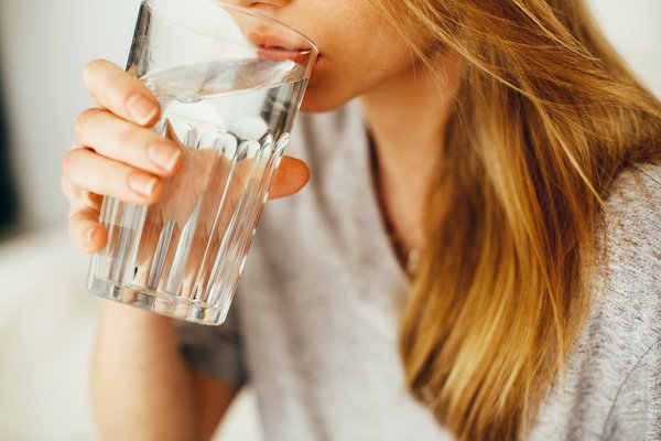 Frau tinkt Wasser aus einem Glas Osmoseanlagen Wasserqualität: Wasserfilter verbessern die Wasserqualität, indem sie Schadstoffe und geschmacksbeeinträchtigende Stoffe entfernen.